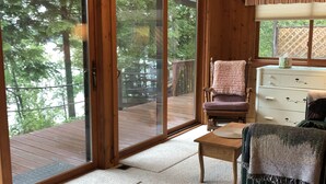 A room with a sliding glass door leading to a wooden deck, a ceiling fan, a wooden dresser, and a chair with a blanket. - Fence Lake Retreat w/ dock (Lac du Flambeau)