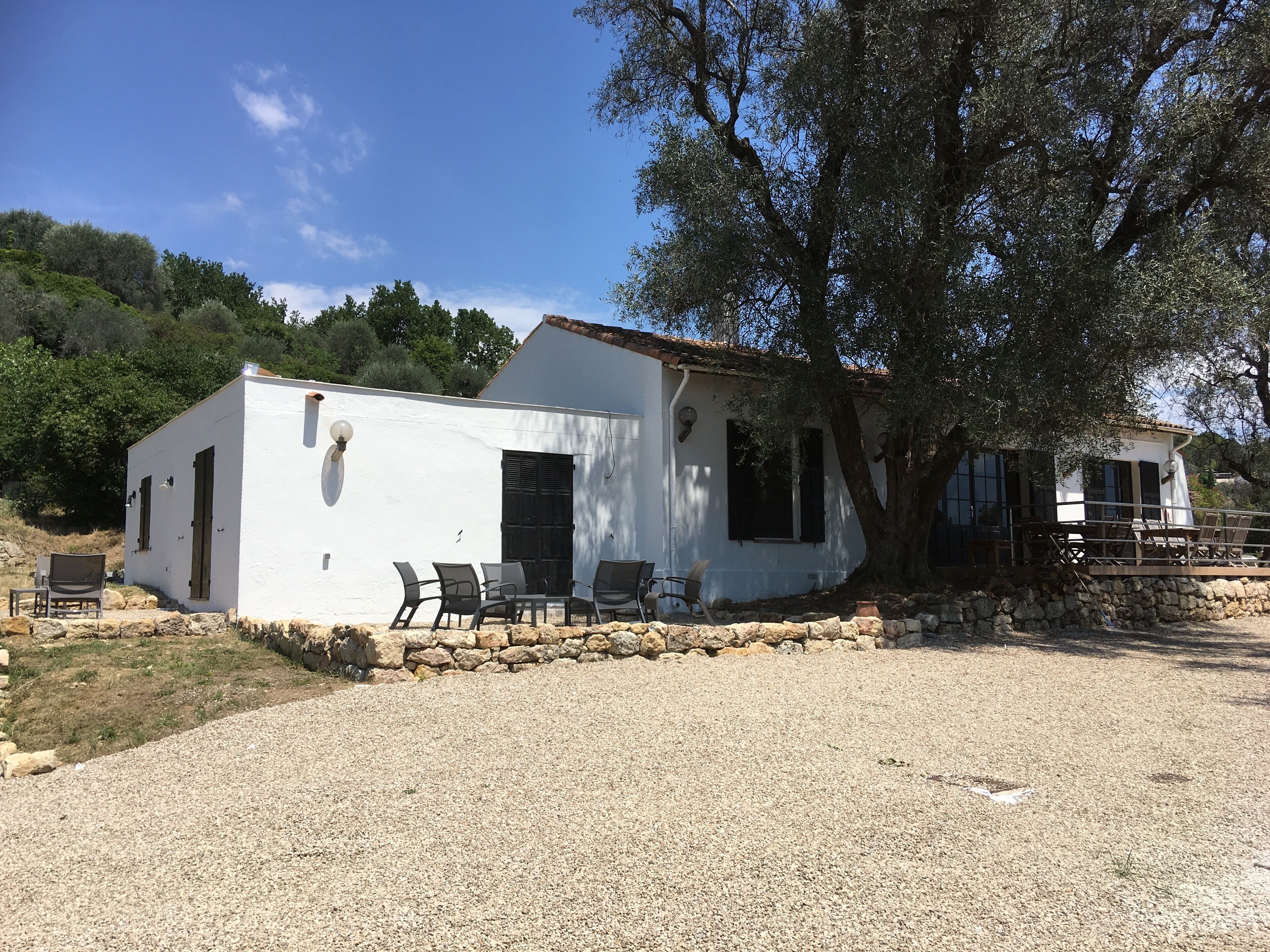 Un edificio blanco con camino de grava, mobiliario exterior y un gran árbol.