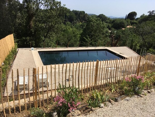 A rectangular swimming pool with a wooden fence and a few lounge chairs.