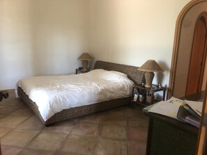 A bedroom with a wicker bed, two bedside lamps, a wooden nightstand, and a green desk with papers.