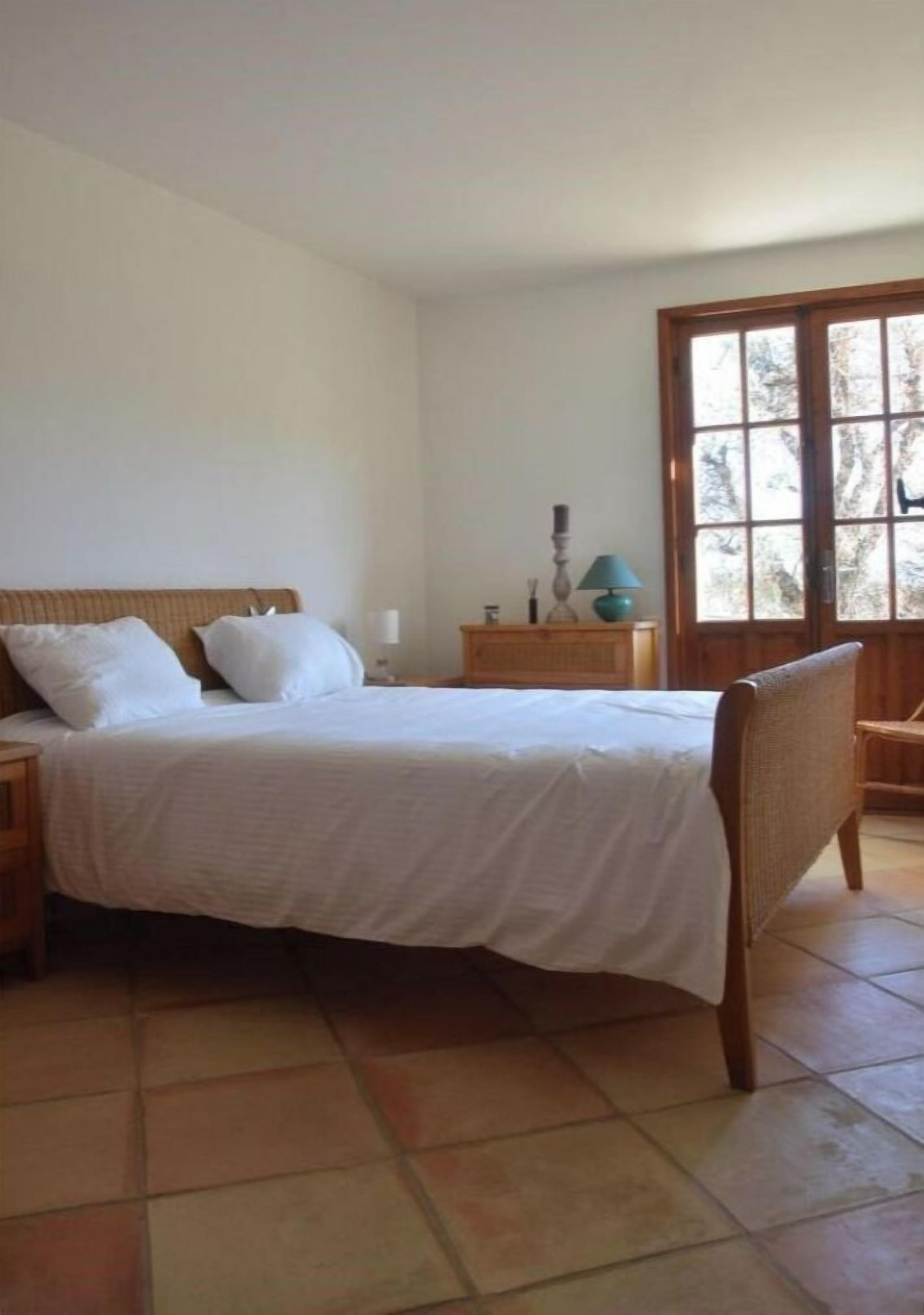 Un dormitorio con cama, mesitas de noche, una silla y una ventana.