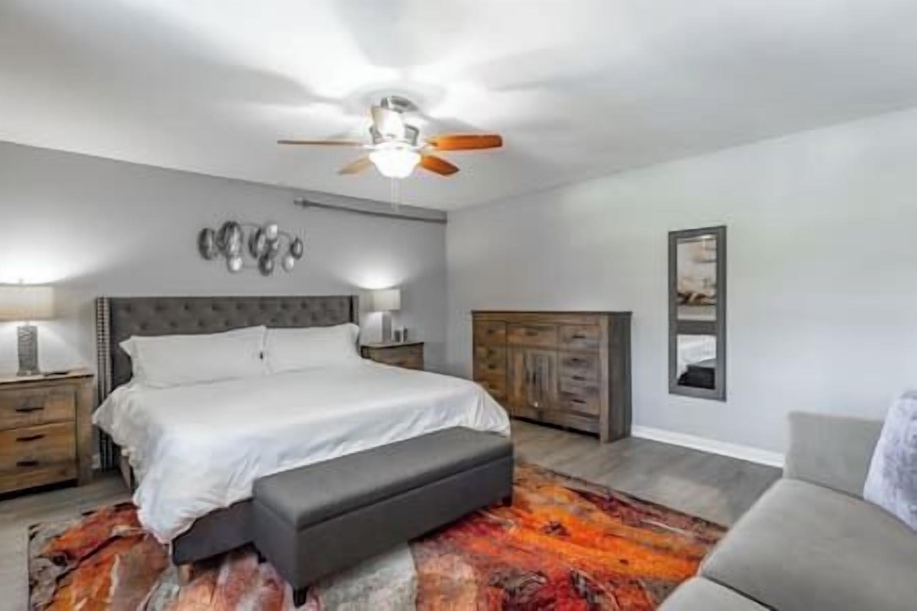 A bedroom with a bed, a bench, a ceiling fan, a dresser, and a mirror.