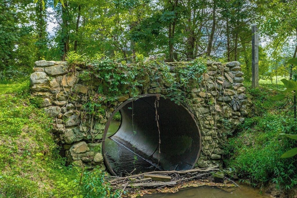 A stone structure with a circular opening, surrounded by lush greenery and trees.