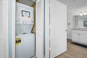 Un cuarto de lavado con lavadora y secadora de carga frontal, una puerta con un letrero y un baño con lavamanos y espejo.