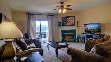 A living room with a fireplace, a ceiling fan, a television, and a view of the outdoors.