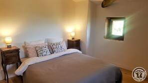 Un dormitorio con una cama, dos mesitas de noche con lámparas, una ventana y un tragaluz pequeño.