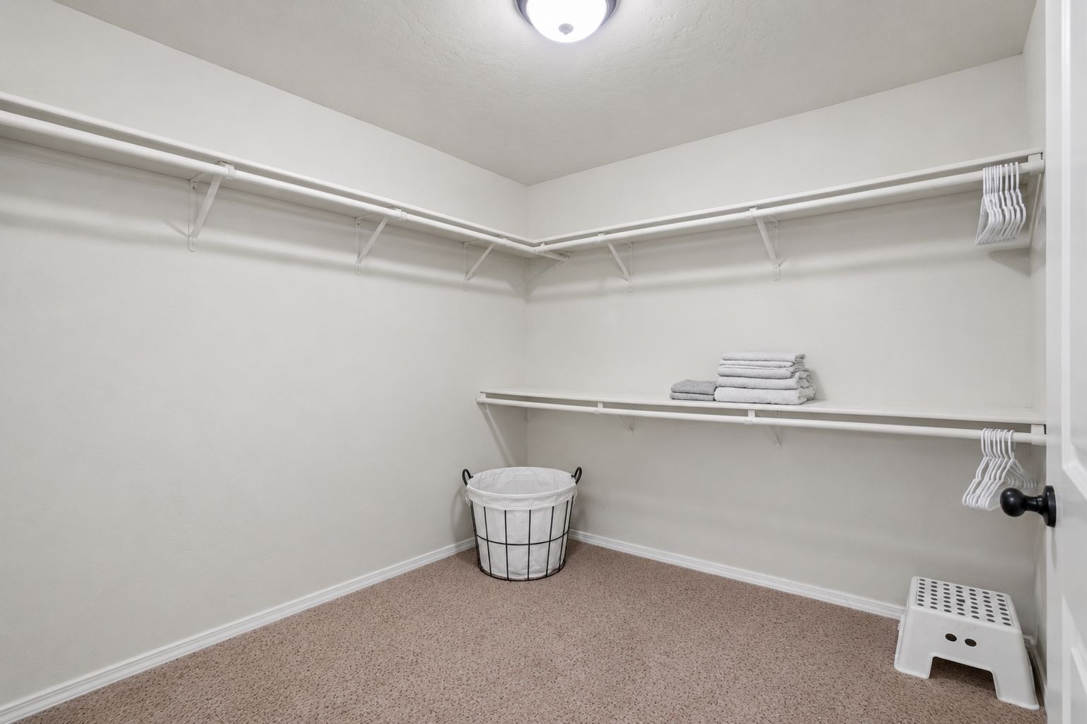 A corner laundry room with a white bucket, shelves for towels, and a small step stool.