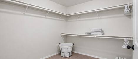 A corner laundry room with a white bucket, shelves for towels, and a small step stool.