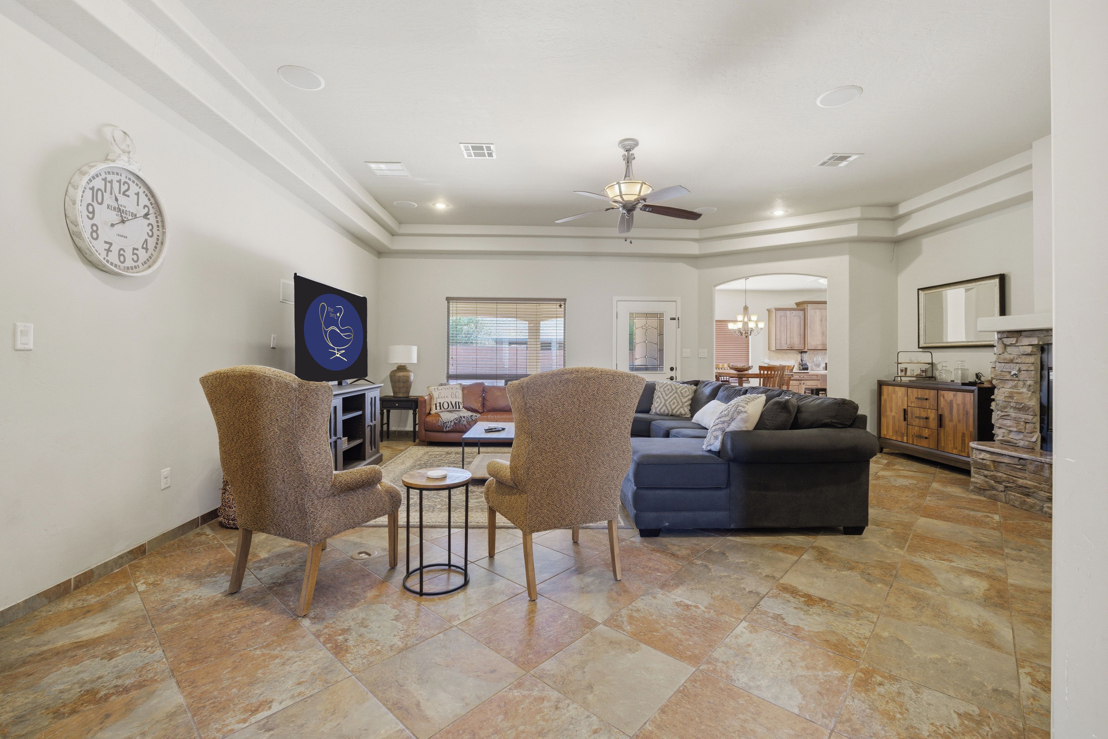 A spacious living room with a dark-colored sofa, two patterned armchairs, a small round table, and a television.