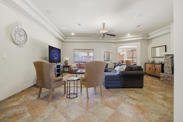 A spacious living room with a dark-colored sofa, two patterned armchairs, a small round table, and a television.