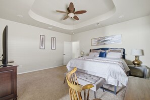 A bedroom with a bed, a desk, a chair, a ceiling fan, and framed artwork on the walls.
