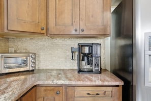 A kitchen with wooden cabinets, a toaster, a coffee maker, and a refrigerator.