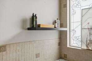 Une salle de bain avec un mur carrelé, une étagère contenant des articles de toilette et une fenêtre ornée de vitraux.