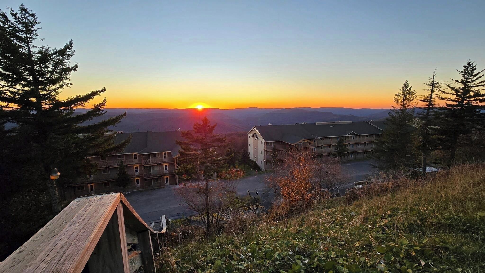 Eine Berglodge mit mehreren Gebäuden, ein Holzbau im Vordergrund und Blick auf den Sonnenuntergang.