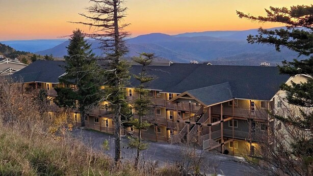 A lodge with multiple wooden buildings, a prominent pine tree, and a mountainous backdrop. - 5 min walk to village and slopes! Peaceful 3 BR 2 Bath retreat (Snowshoe)