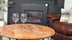 A round wooden table with two wine glasses on it, a leather couch with striped pillows, and a fireplace in the background. - 5 min walk to village and slopes! Peaceful 3 BR 2 Bath retreat (Snowshoe)