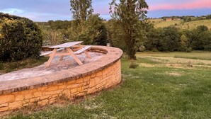 Un banco de piedra con una mesa de picnic en un área verde con árboles y colinas al fondo.