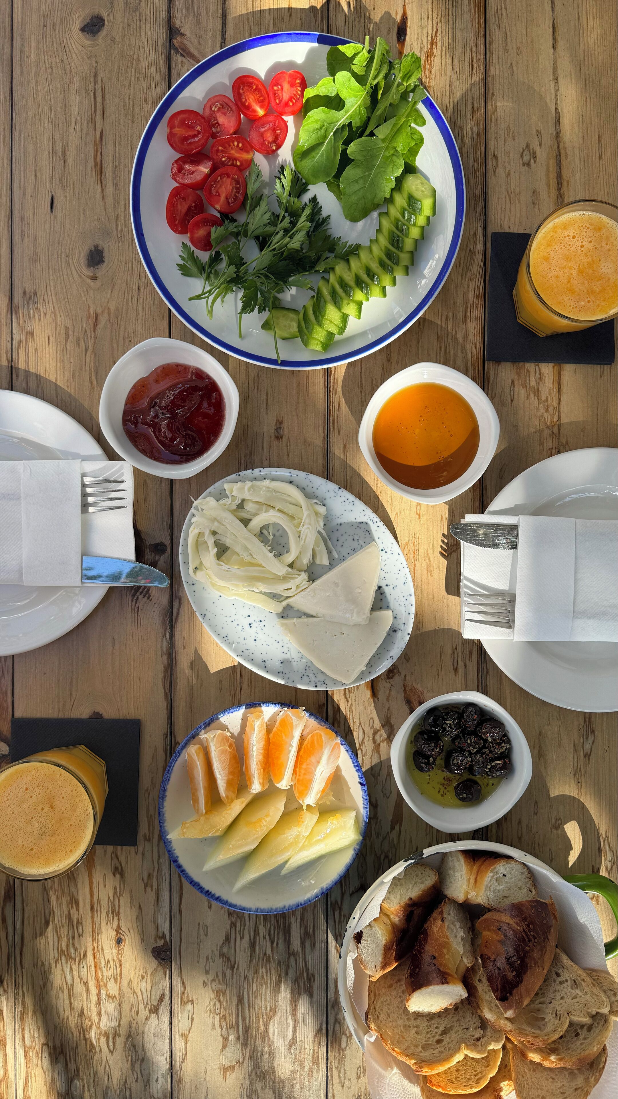 Une table en bois sur laquelle on trouve divers aliments, notamment des tomates en tranches, des concombres, du fromage, du pain et des boissons.