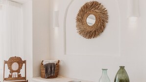 Un interior moderno con una pared blanca, una silla de madera, una cesta tejida y dos taburetes.