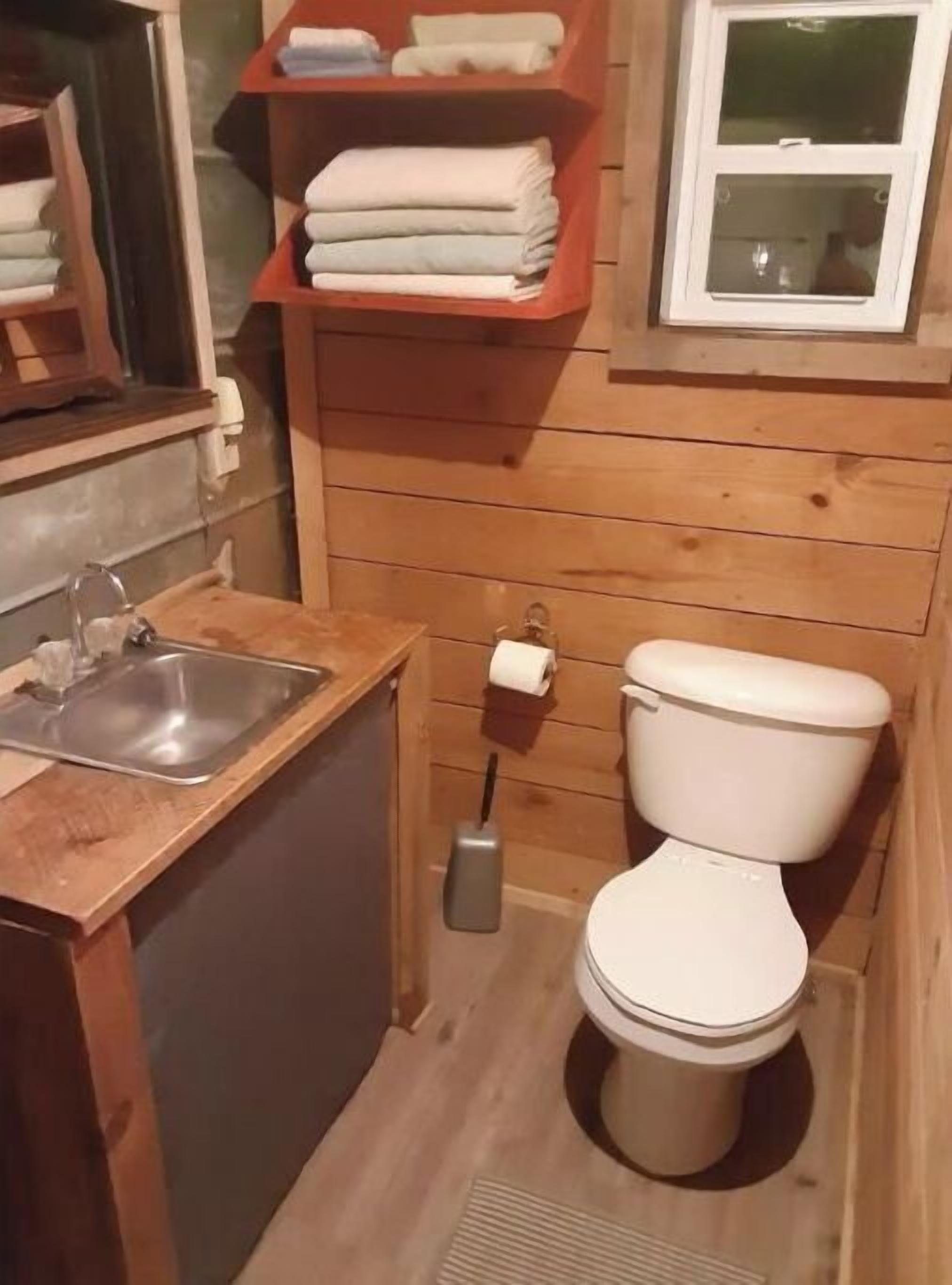 A compact bathroom with a sink, toilet, and shelves with folded towels.