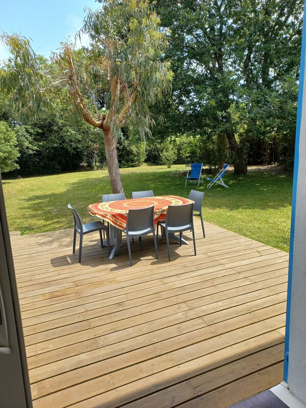 A wooden deck with a round table and chairs, surrounded by greenery and trees.
