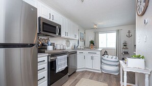 A modern kitchen with stainless steel appliances, white cabinetry, and a small dining area with a wicker basket and a clock on the wall.