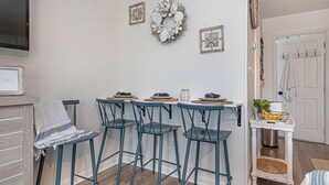 A kitchen with four blue bar stools, a white wall with a wreath, and a small white table with a basket.