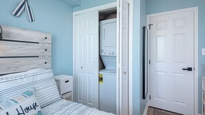 A bedroom with a bed, a nightstand, a closet with a washing machine, and a door.