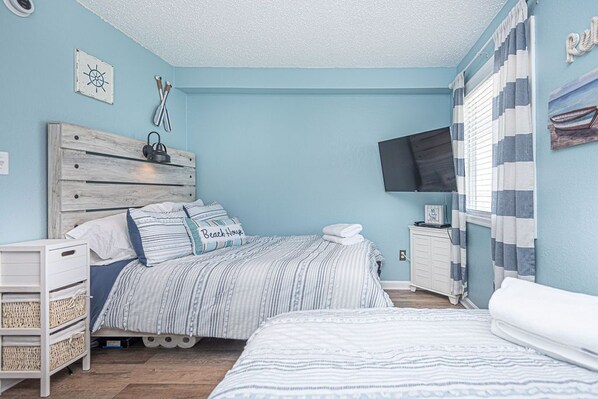 Un dormitorio con cama, mesita de noche, televisor y ventana con cortinas.