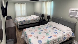 A hotel room with two beds, each with a sea-themed bedspread, a desk with a chair, a TV mounted on the wall, and a ceiling fan. - Crystal Beach Cozy Cottage - Your Perfect Vacation Escape! (Palm Harbor)