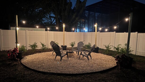 A circular outdoor seating area with four Adirondack chairs and a small table, surrounded by a white fence and potted plants. - Crystal Beach Cozy Cottage - Your Perfect Vacation Escape! (Palm Harbor)