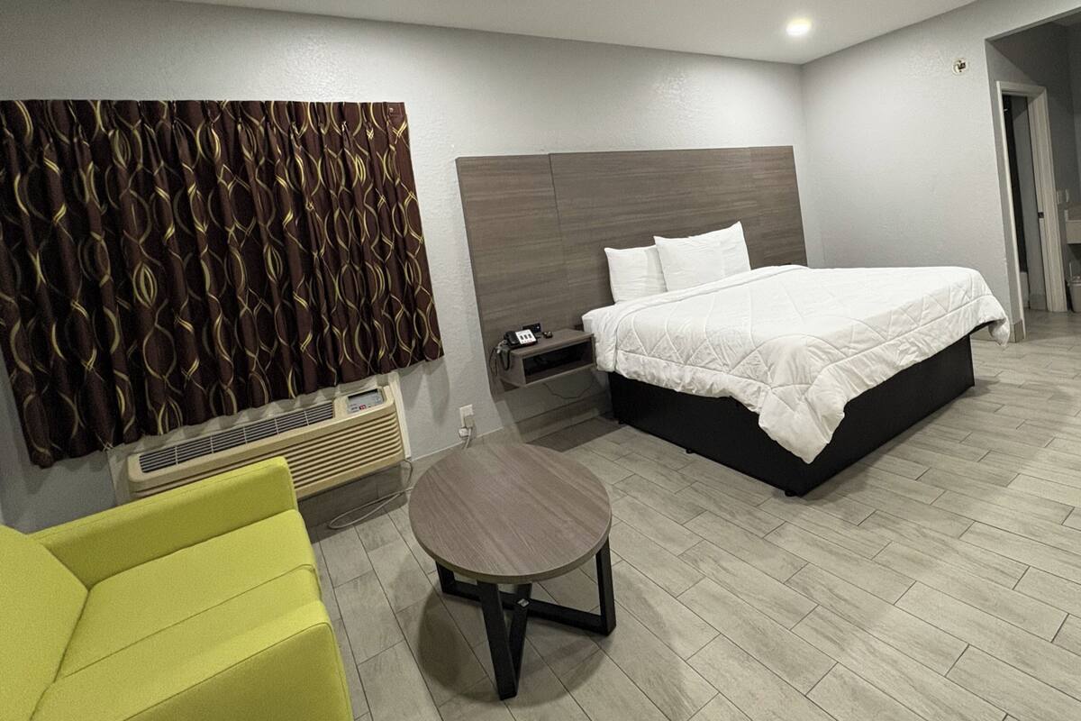 A modern hotel room with a large bed, a bedside table, a chair, and a decorative wall panel.