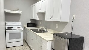 A compact kitchen with white cabinets, a stainless steel refrigerator, a microwave, and a stove. - Kiwi Inn Capital O Houston - Hwy 249 (Houston)