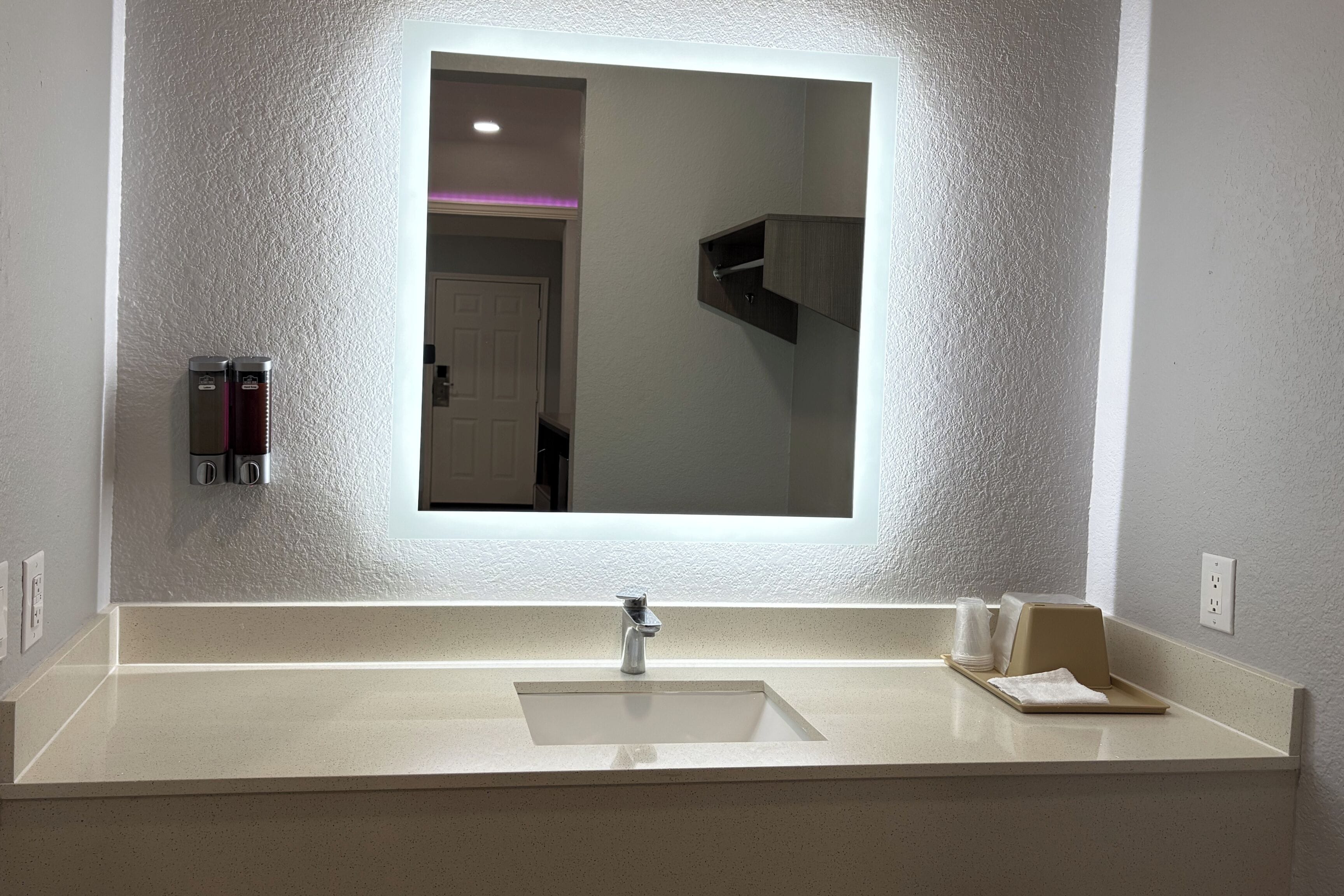 A bathroom with a large mirror, a sink, and a towel rack.