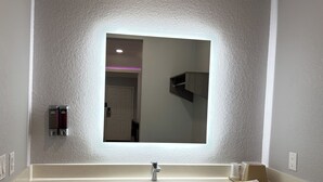 A bathroom with a large mirror, a sink, and a towel rack. - Kiwi Inn Capital O Houston - Hwy 249 (Houston)