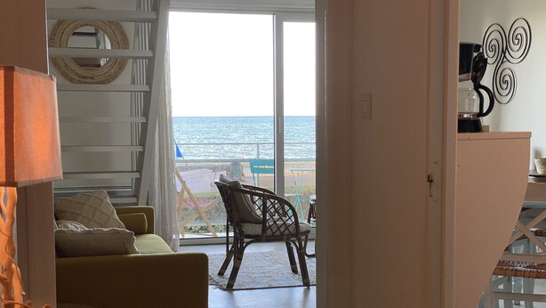 Una habitación con sofá, sillón, lámpara y vistas al mar a través de un ventanal.