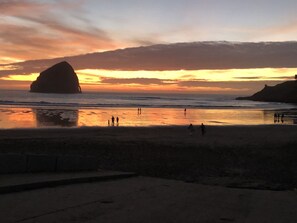 Une scène de plage avec une grande formation rocheuse et des personnes se promenant le long du rivage.