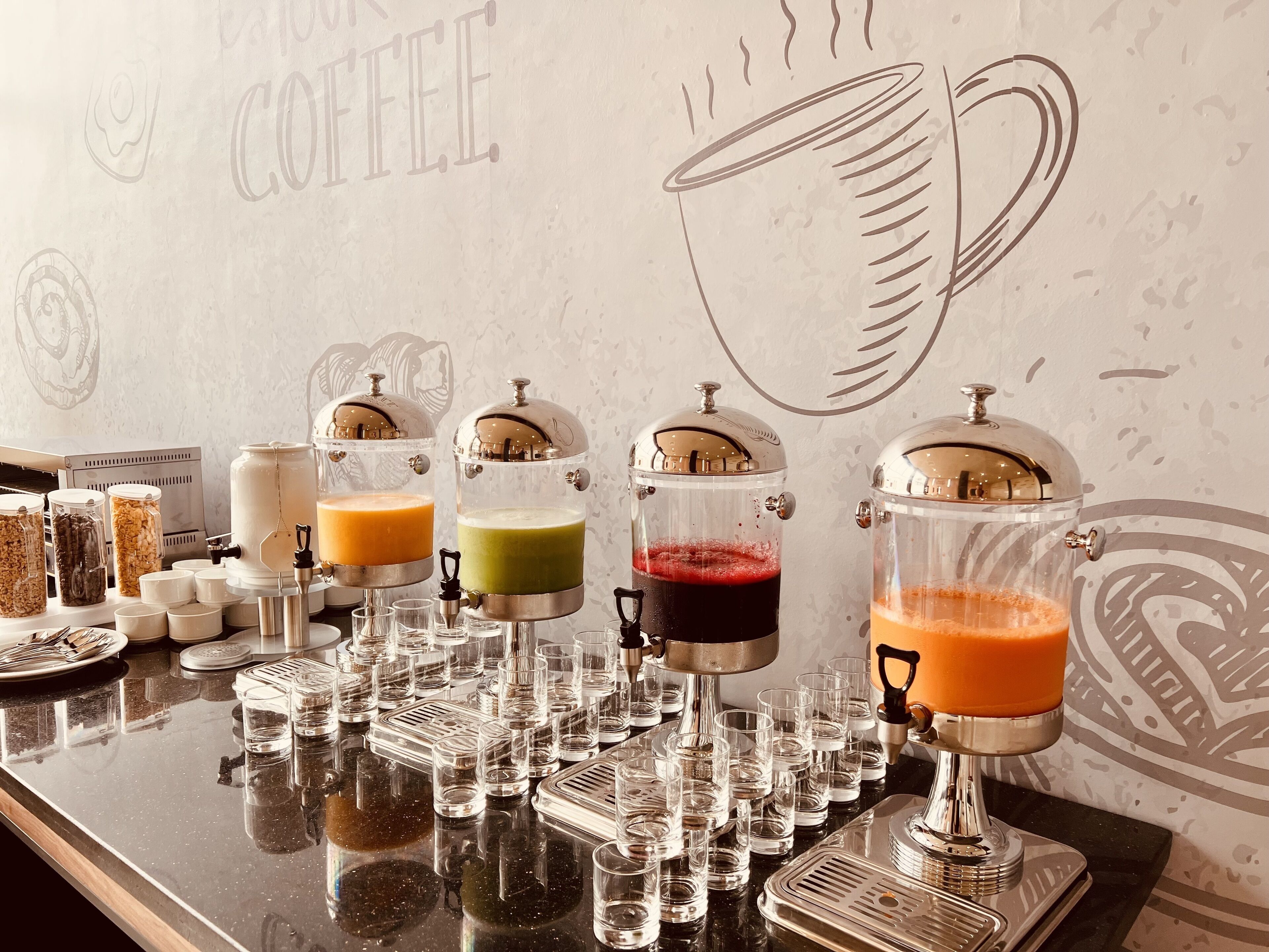 Un espace dédié au café, équipé de plusieurs distributeurs de boissons de différentes couleurs, d’une machine à café et d’un mur décoré avec un motif de tasse à café.