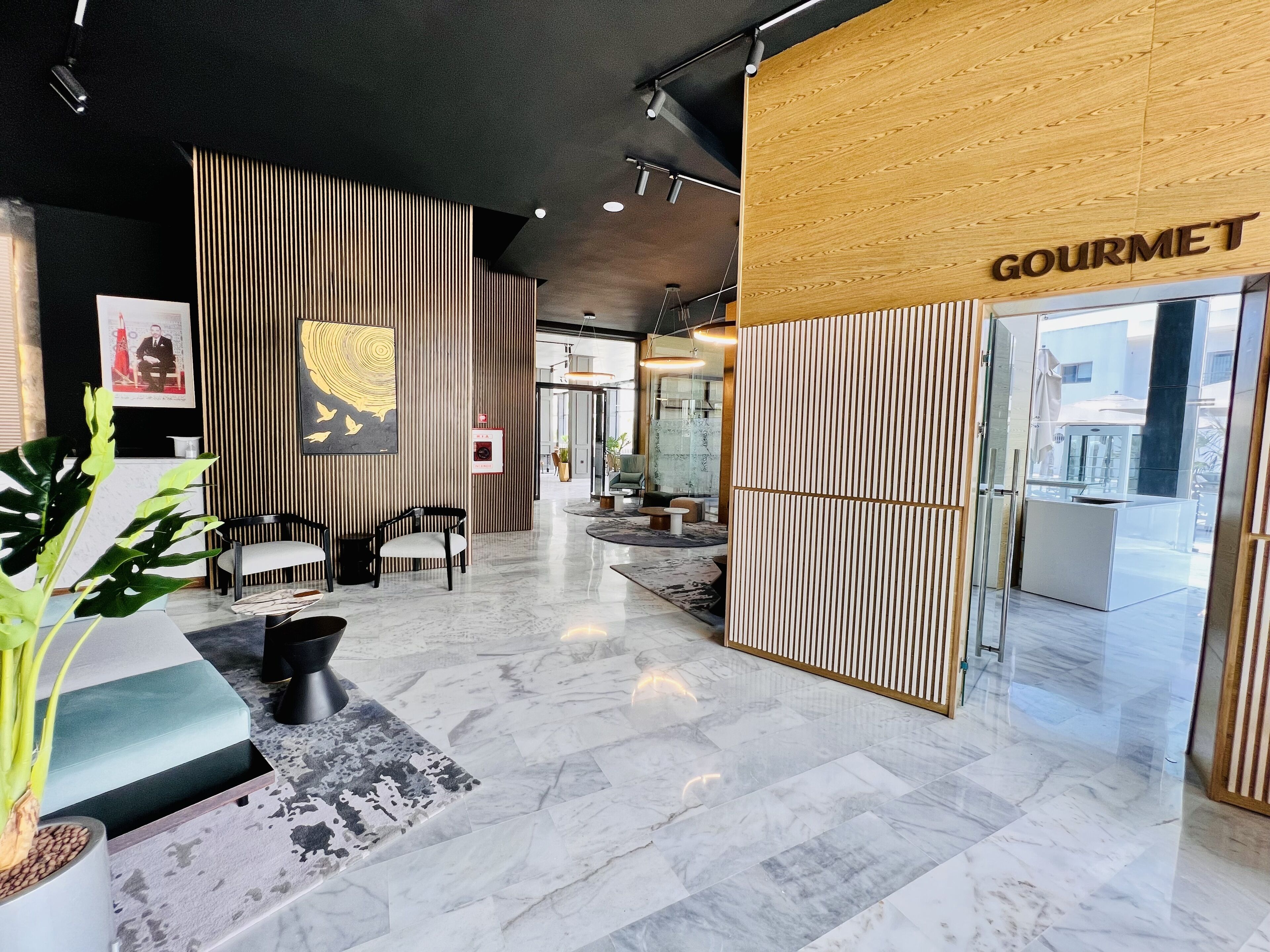 A modern lobby with a reception desk, seating area, and a 'GOURMET' sign.