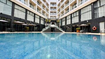 Un hotel moderno con piscina central, varios balcones y zonas de estar al aire libre.