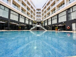 Un hotel moderno con piscina central, varios balcones y zonas de estar al aire libre.