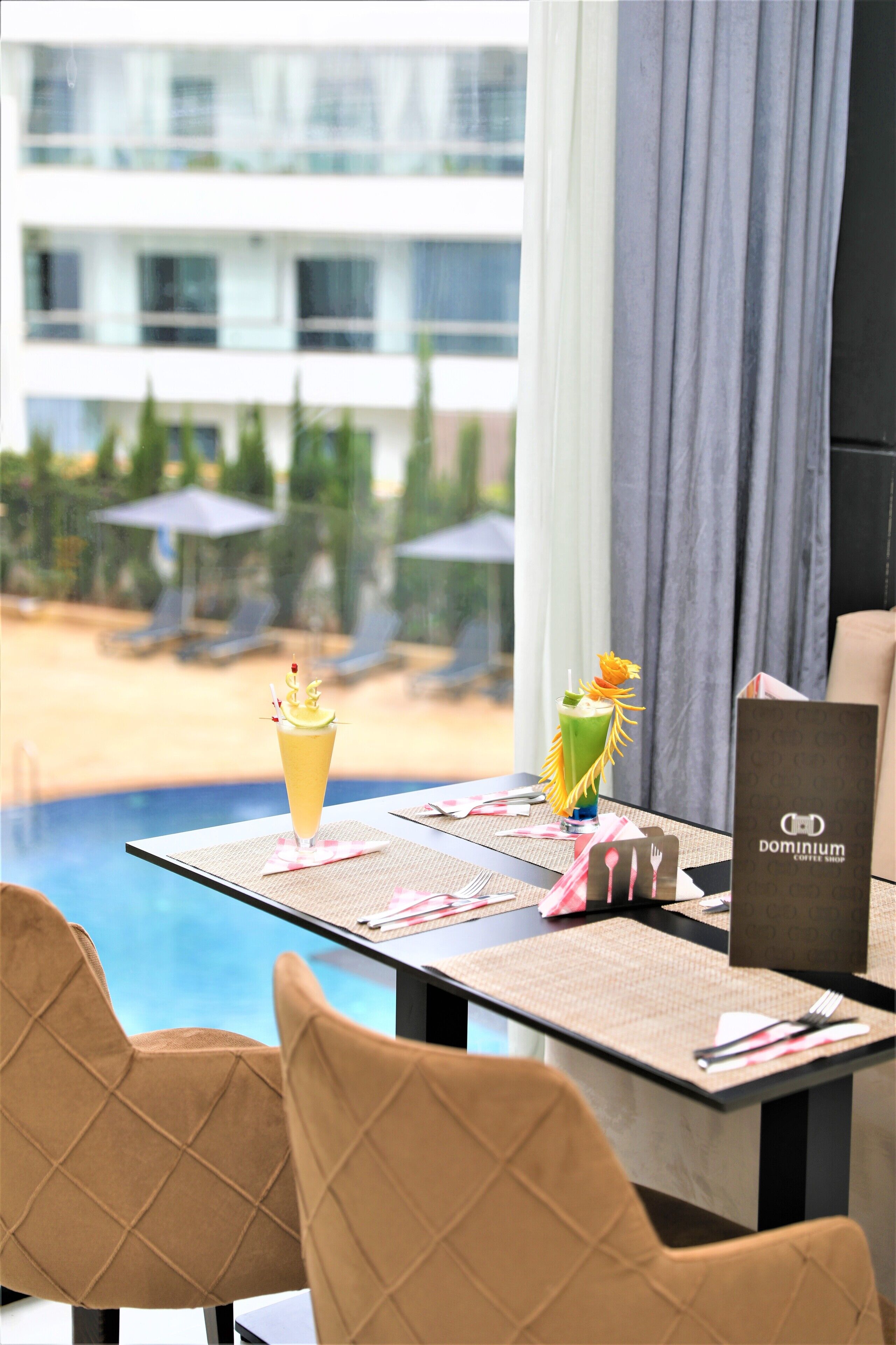 Una mesa de comedor con un menú, dos bebidas y vistas a una piscina y sillas de playa.