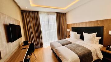 Habitación de hotel con una cama grande, un escritorio, una silla, un televisor y una ventana con cortinas.