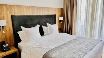 Una habitación de hotel con una cama grande, un cabecero de madera, una mesita de noche con un teléfono y una ventana con cortinas.