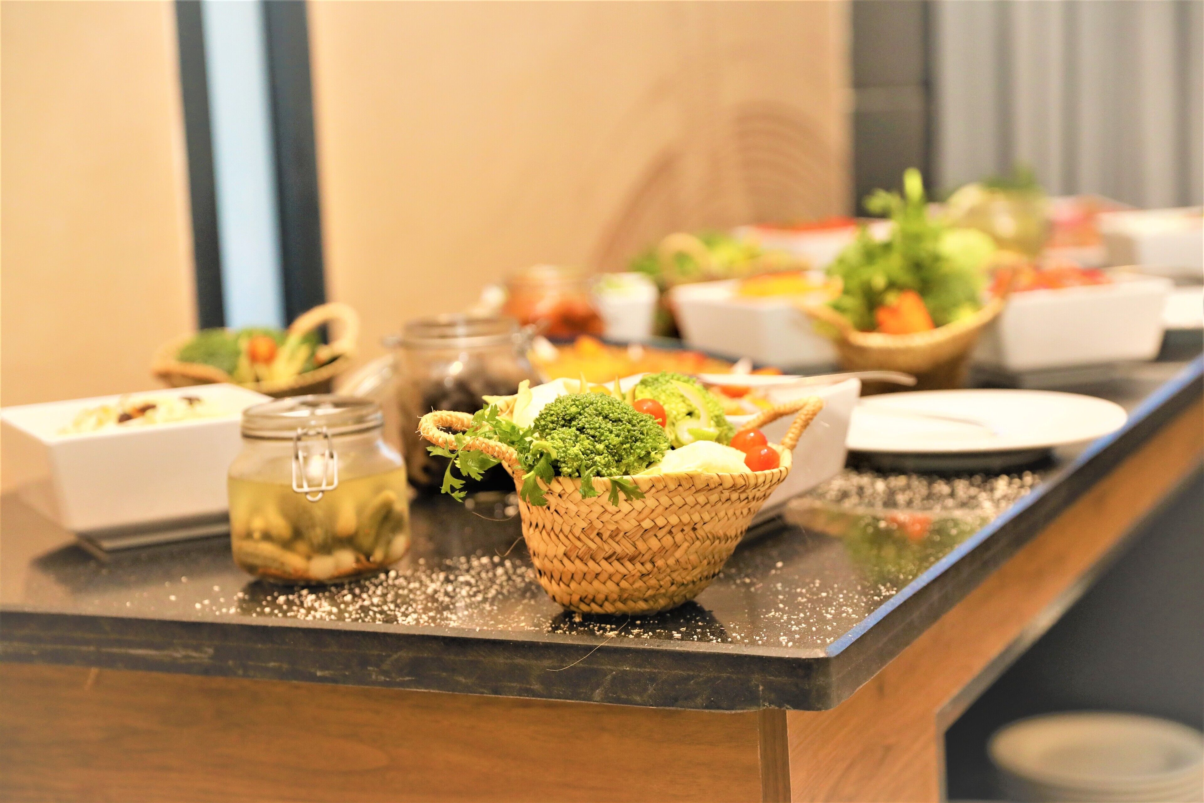 A buffet table with various dishes and a basket of fresh vegetables.