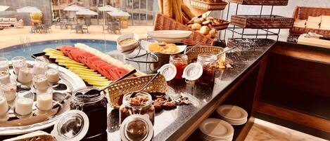A buffet with various food items and beverages, including fruits, bread, and jars of spreads.