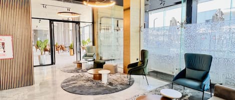 A modern lobby with a circular seating area, a reception desk, and large windows offering a view.