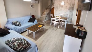 Ein Wohnzimmer mit einer Couch, einem Couchtisch mit Früchten, einem Essbereich mit Stühlen und einer Treppe, die zu einer weiteren Ebene führt.