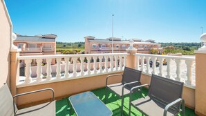 Ein Balkon mit Tisch und Stühlen, Blick auf ein Gebäude mit Ziegeldach und einem strahlend blauen Himmel.