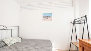 Ein Schlafzimmer mit einem Bett, einer Holzkommode, einem Wäscheständer aus Metall und einem Bild an der Wand.